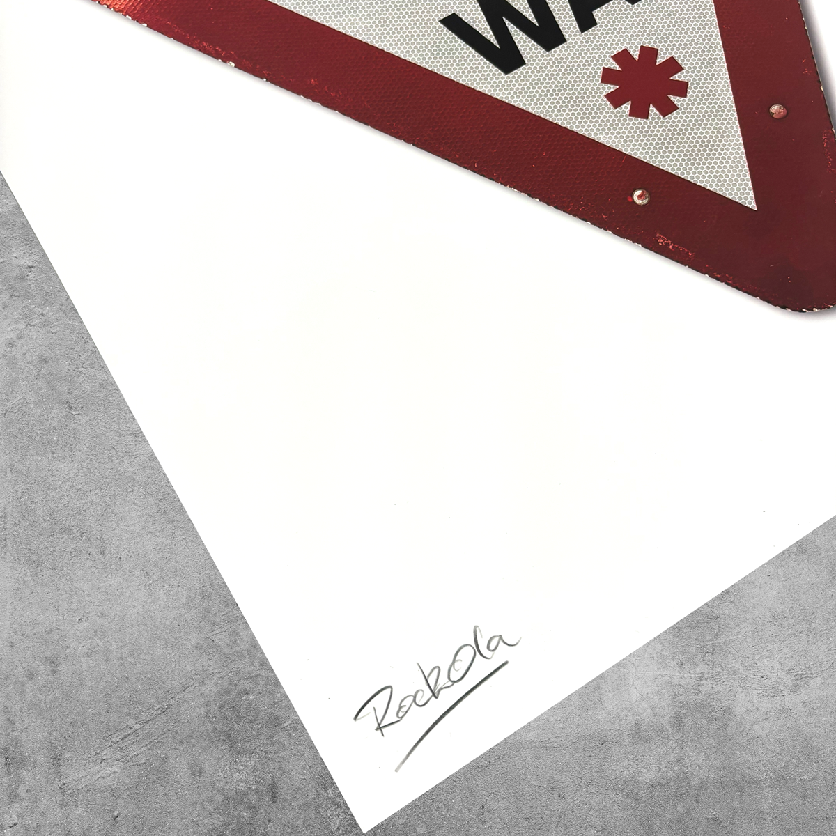 A corner of a red and white UK road sign with an asterisk overlays white paper on gray concrete. RekOla is handwritten below, marking it as the RocknRoad Sign Print - Give It A Way by 45 Original, limited to 25 editions.