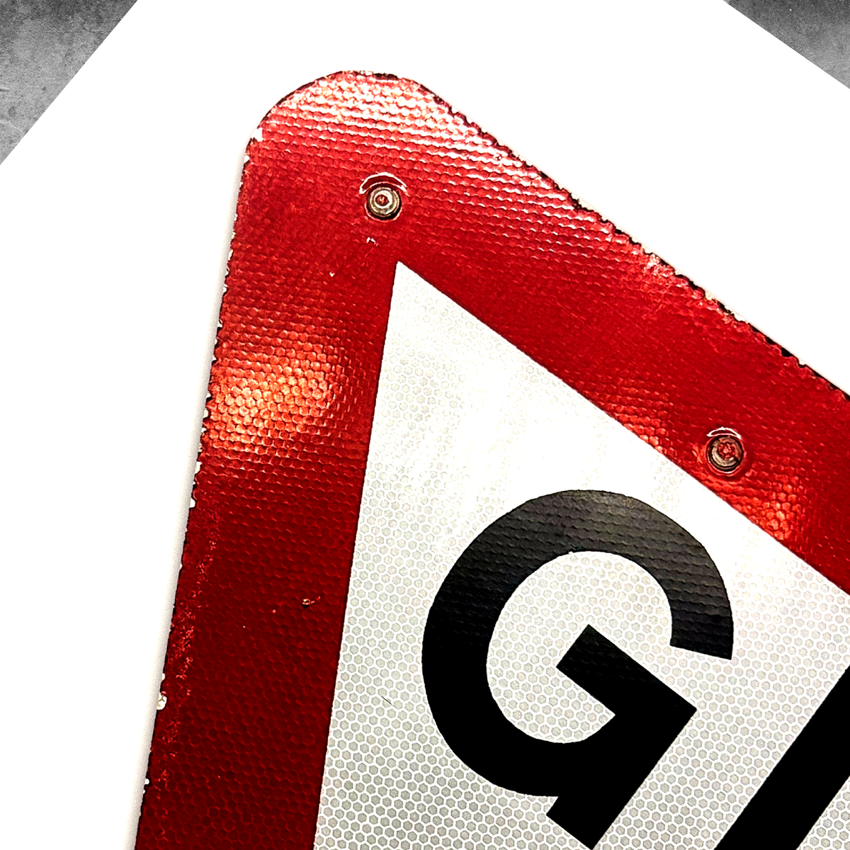 A close-up of a UK road sign corner from 45 Original’s RocknRoad Sign Print - Give It A Way (Limited Edition of 25), featuring bold black lettering on white with a red border—perfect as a striking giclée or collectible print.