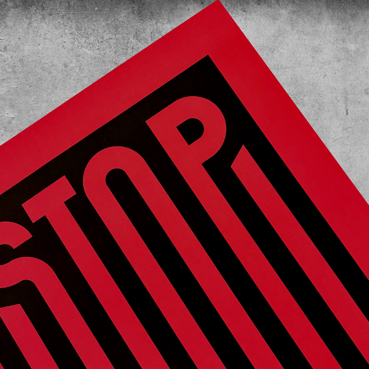 A close-up, angled view of ‘Stop War’ Red And Black Print—Limited Edition of only 250—with bold “STOP” lettering visible against a grey concrete background in an impactful style.