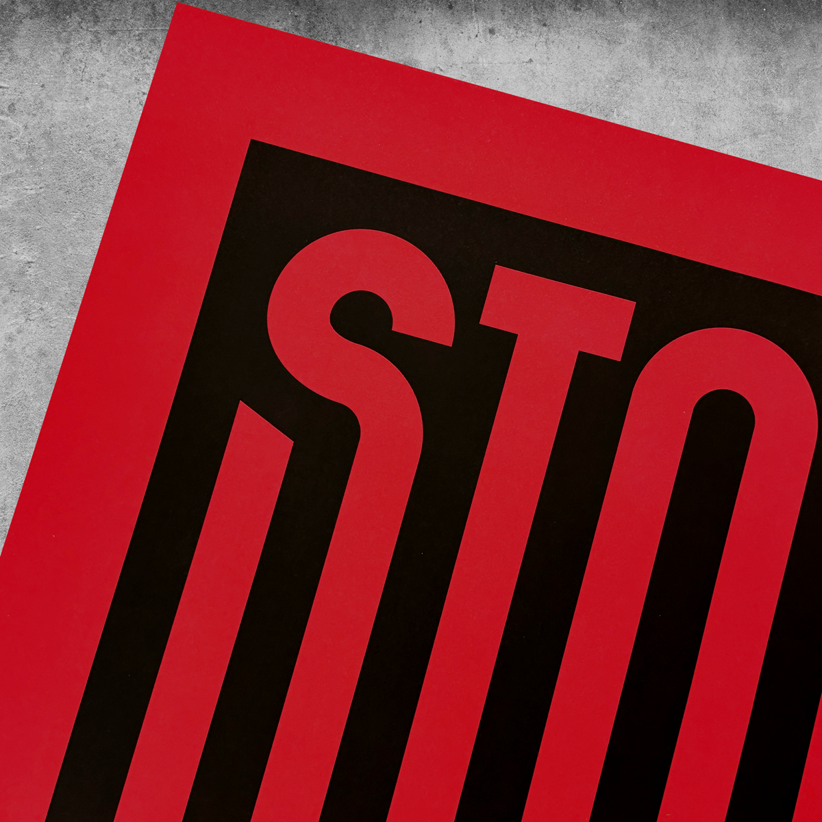 A close-up of ‘Stop War’ Red And Black Print (limited edition of 250) showcases bold black letters “STO” in a modern font on red, set against a textured gray background.