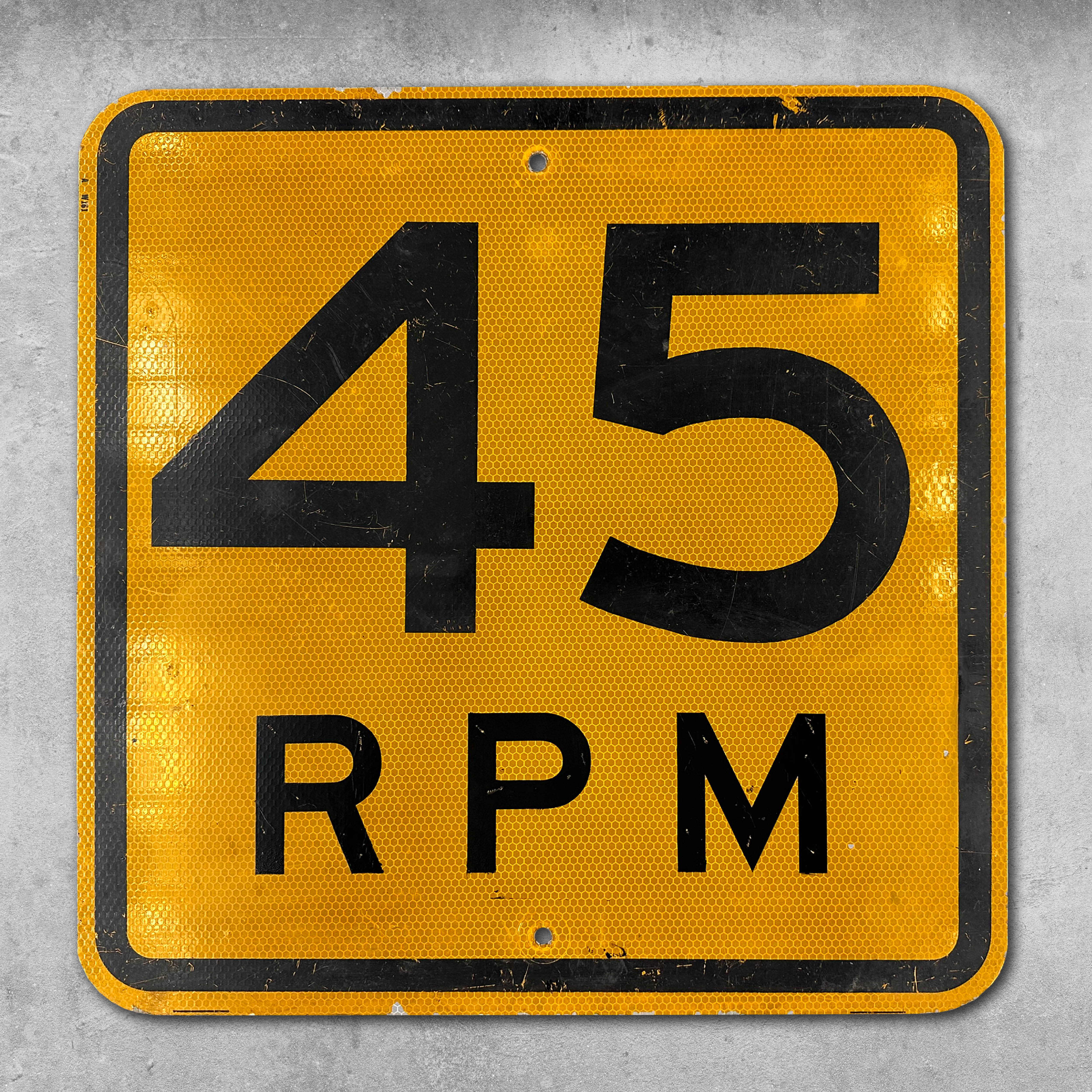 The My Store Original RocknRoad Sign - Yellow 45 RPM is a square metal sign with rounded edges, featuring a bold black 45 RPM on yellow. Slightly scratched and worn, its perfect for home sound system decor or any RocknRoll collection.