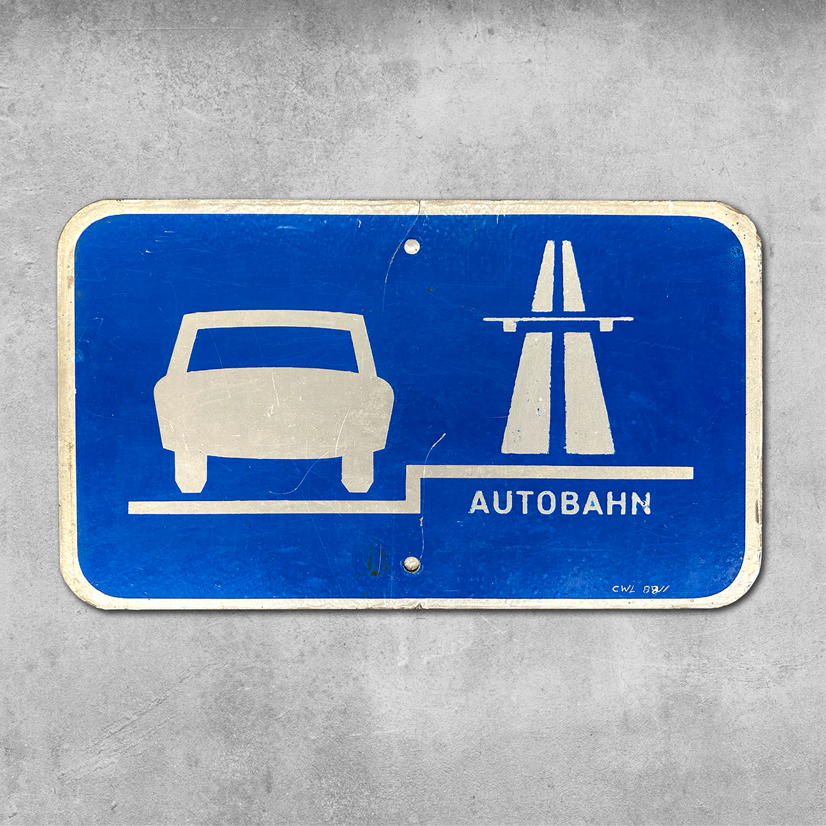 The Original RocknRoad Sign - Autobahn II by 45 Original is a blue sign with a white Trabant-style car, a stylized highway symbol, and AUTOBAHN, mounted on concrete and displaying an amazing patina.