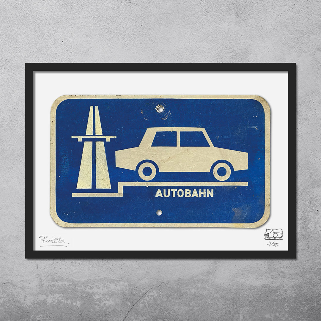 The RocknRoad Sign Print - Autobahn by My Store is a limited edition framed giclée print (25 available), featuring a blue and white East German-style road sign with car and highway icon, AUTOBAHN below, displayed on a gray concrete wall.
