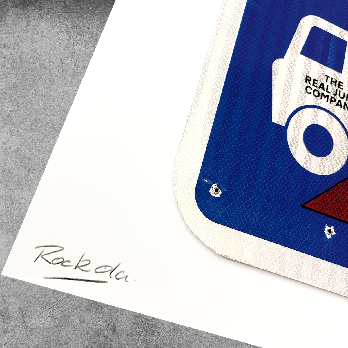 A close-up of the RocknRoad Sign Print - Garbageman by 45 Original, a limited edition of 25, shows a blue and white street sign on white with a handwritten Rackola signature. Offered as a full-color giclée print on textured gray surface.