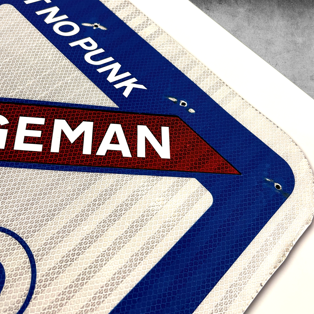 The RocknRoad Sign Print - Garbageman from 45 Original captures a striking close-up of a “NO PUNK” street sign on a blue, white, and red background. This limited-edition giclée print highlights the sign’s reflective texture and metal bolts.