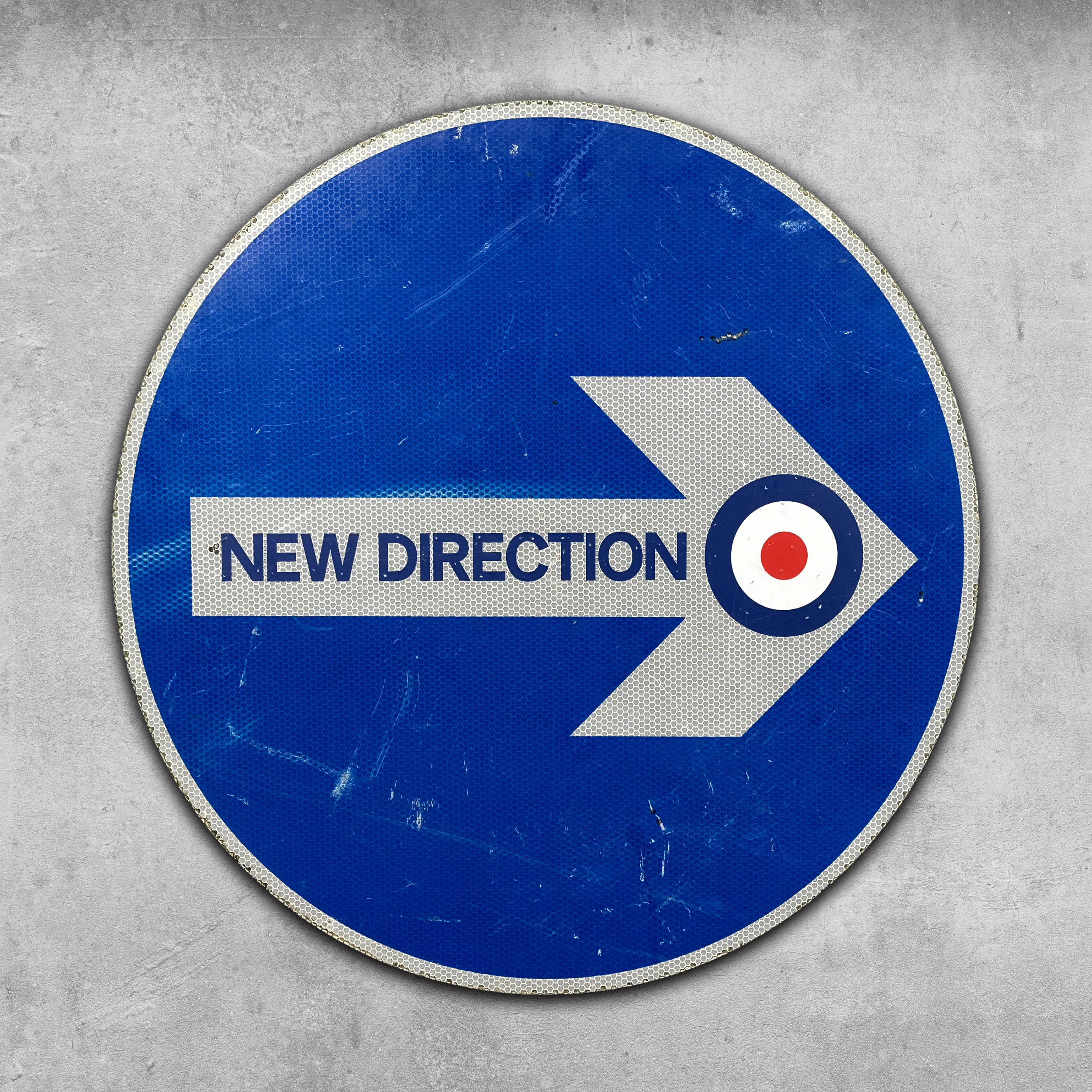 The Original RocknRoad Sign - New Direction by My Store features a blue circular Modernist UK metal design with a white right arrow, NEW DIRECTION text, and a red, white & blue roundel tip. Its shown mounted on a textured gray wall.