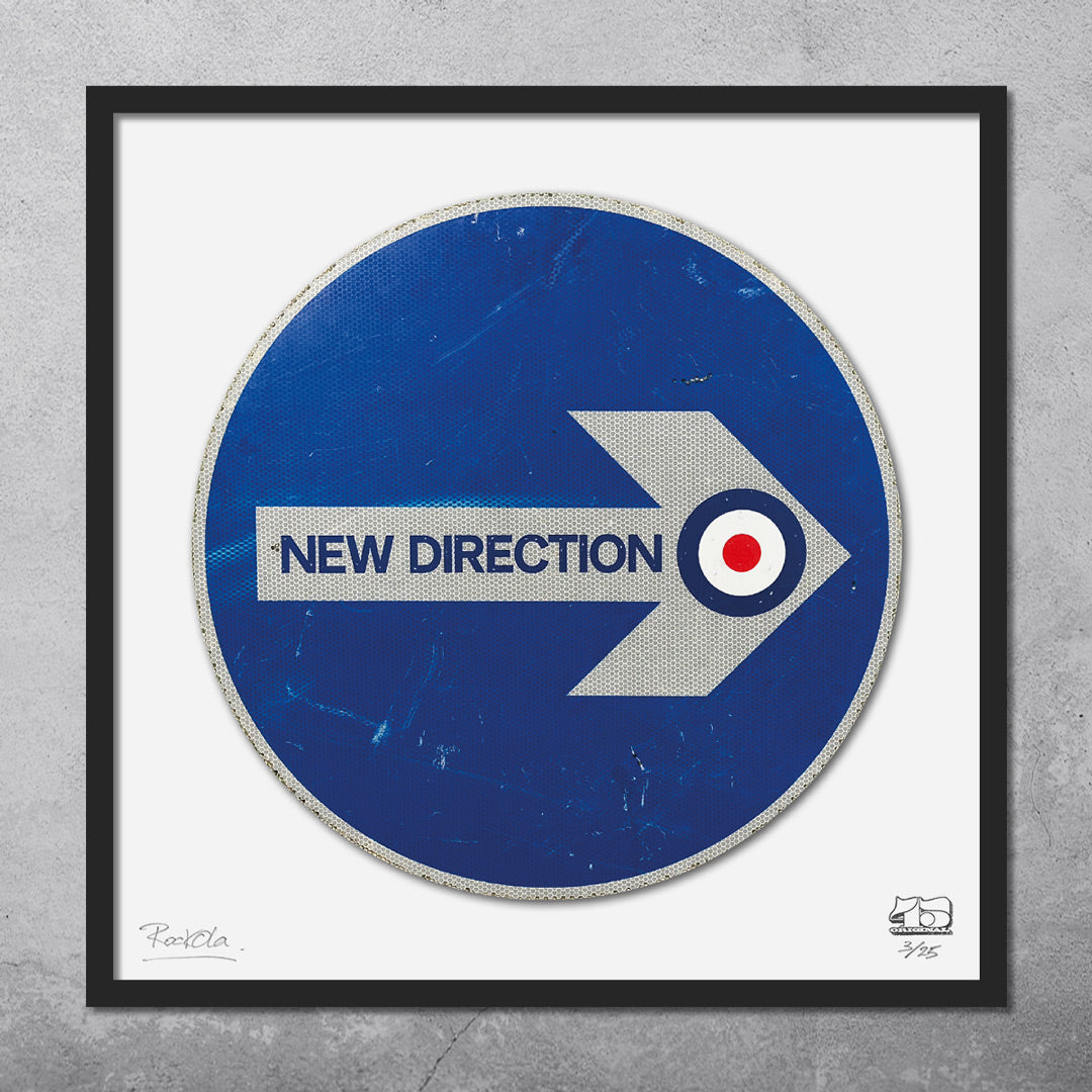 The RocknRoad Sign Print - New Direction by My Store is a limited edition framed giclée featuring a blue right-arrow road sign, NEW DIRECTION text, and target symbol on a textured concrete wall—ideal for modernist décor.